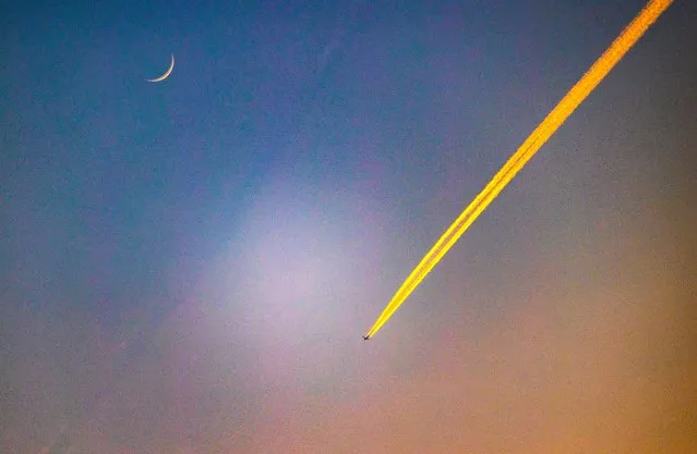 A plane flies west over Berkshire, United Kingdom on May 22, 2023 beneath a new moon. (Photo by David Hartley/Rex Features/Shutterstock)
