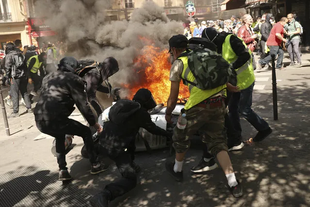 Demonstrators attend to a motorbike which was set alight during a yellow vest demonstration in Paris, Saturday, April 20, 2019. French yellow vest protesters are marching anew to remind the government that rebuilding the fire-ravaged Notre Dame Cathedral isn't the only problem the nation needs to solve. (Photo by Francisco Seco/AP Photo)