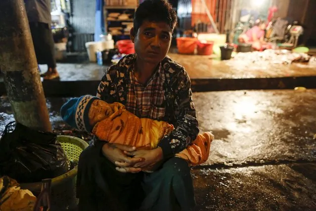 A vendor holds his baby as he waits for a bus after bringing fish to sell at San Pya fish market, in Yangon, Myanmar February 15, 2016. (Photo by Soe Zeya Tun/Reuters)