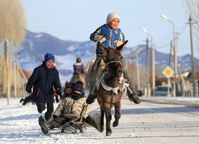 Children ride a sled pulled by a donkey in the village of Karasaz in Almaty Region, Kazakhstan on December 4, 2021. (Photo by Pavel Mikheyev/Reuters)