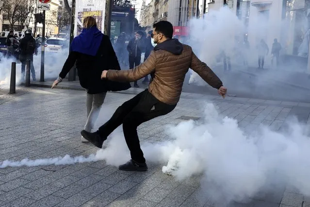 A demonstrator kicks in a tear gas grenade during a protest on the Champs-Elysees avenue, Saturday, February 12, 2022 in Paris. Paris police intercepted at least 500 vehicles attempting to enter the French capital in defiance of a police order to take part in protests against virus restrictions inspired by the Canada's horn-honking “Freedom Convoy”. (Photo by Adrienne Surprenant/AP Photo)