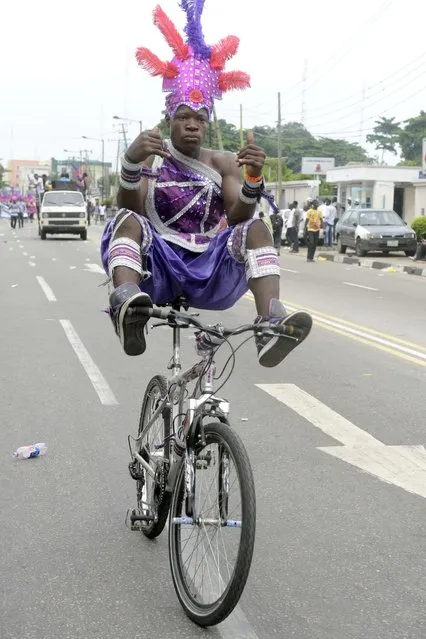 A boy entertains bystanders with his bicycle during a procession at the yearly Lagos carnival to mark the Easter holiday on April 21, 2014. The carnival was held with processions combining some elements of a circus, grand display of fabulous costumes by the participants, and public street parties at various locations where the parade took place. (Photo by Pius Utomi Ekpei/AFP Photo)