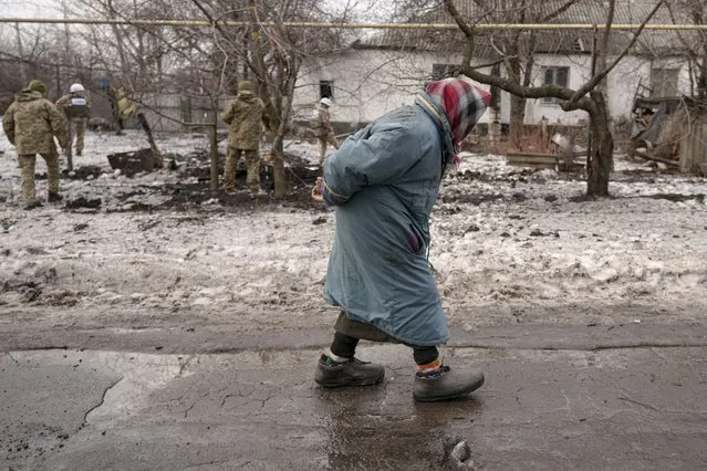 An elderly lady walks by as members of the Joint Centre for Control and Coordination on ceasefire of the demarcation line, or JCCC, survey a crater and damage to a house from artillery shell that landed in Vrubivka, one of the at least eight that hit the village today, according to local officials, in the Luhansk region, eastern Ukraine, Thursday, February 17, 2022. U.S. President Joe Biden warned that Russia could still invade Ukraine within days and Russia expelled the No. 2 diplomat at the U.S. Embassy in Moscow, as tensions flared anew in the worst East-West standoff in decades. (Photo by Vadim Ghirda/AP Photo)