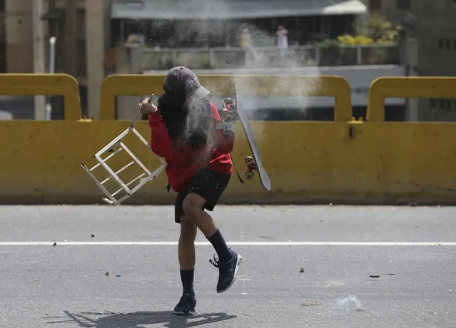 A demonstrator protects himself after a tear gas canister fired by police riot crashed against his skateboard during a protest in Caracas, Venezuela, Thursday, April 6, 2017. (Photo by Fernando Llano/AP Photo)