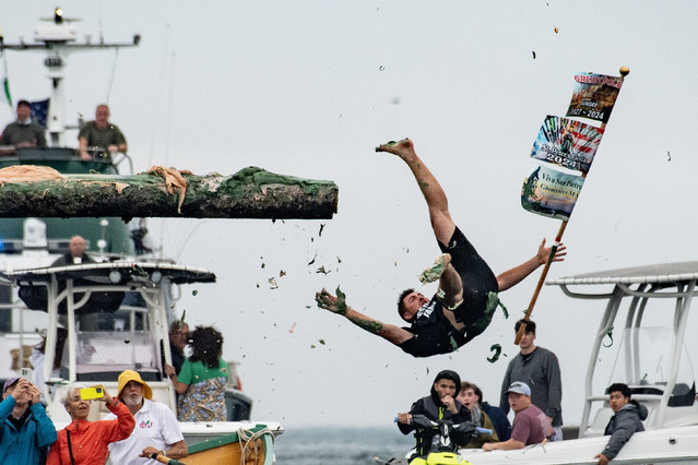 Past Champion Derek Hopkins flies through the air with the flag close at hand during the 94th annual Sunday Greasy Pole contest at St. Peter's Fiesta in Gloucester, Massachusetts, United States on June 30, 2024. The greasy pole contest is sponsored by the Italian-American fishing community of Gloucester and started in 1931. St. Peter's fiesta started in 1927. (Photo by Joseph Prezioso/Anadolu via Getty Images)