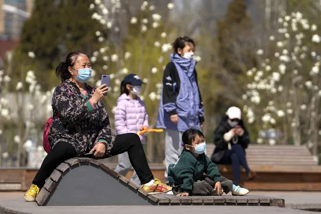 Residents wearing face masks to help protect from the coronavirus bring their children for sunbathing outside a mall, Sunday, April 3, 2022, in Beijing. COVID-19 cases in China's largest city of Shanghai are still rising as millions remain isolated at home under a sweeping lockdown. (Photo by Andy Wong/AP Photo)