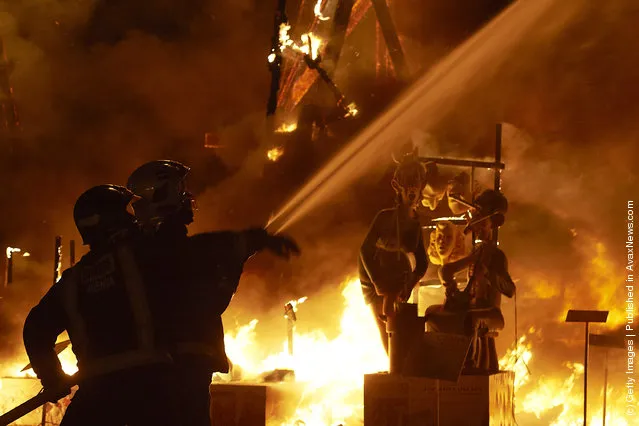 A fireman sprays water while a combustible 'Ninot' caricature burns in the background during the last day of the 'Fallas' festival on March 19, 2012 in Valencia, Spain