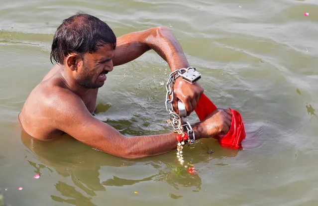 A man, whose relative says suffers from mental illness and is chained to prevent him from running away, tries to open a lock on his chained hands as he takes a dip in the waters of the Ganges river during Jyestha Purnima or full moon of Jyestha month in Allahabad, India June 9, 2017. (Photo by Jitendra Prakash/Reuters)