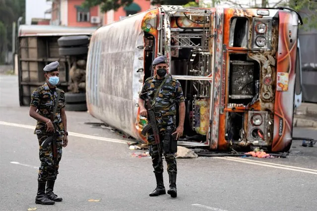Sri Lankan soldiers stand guard next to burnt buses a day after clashes between government supporters and anti-government protesters in Colombo, Sri Lanka, Tuesday, May 10, 2022. Defying a nationwide curfew in Sri Lanka, several hundred protesters continued to chant slogans against the government Tuesday, a day after violent clashes saw the resignation of the prime minister who is blamed, along with his brother, the president, for leading the country into its worst economic crisis in decades. (Photo by Eranga Jayawardena/AP Photo)