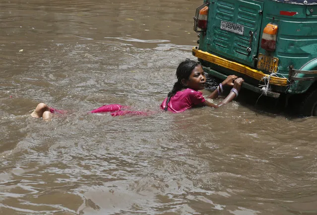 An Indian girl holds on to the back of an auto-rickshaw as she plays in a flooded street with other children after a heavy monsoon rain in Ahmadabad, India, Tuesday, July 18, 2017. The monsoon season runs in India from June to September. (Photo by Ajit Solanki/AP Photo)