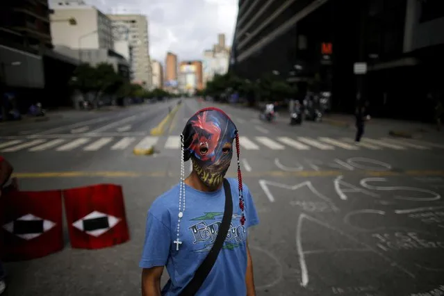 A demonstrator wearing a mask adorned with rosaries stands near a barricade during a 48-hour general strike beginning Wednesday in protest of government plans to rewrite the constitution in Caracas, Venezuela, Wednesday, July 26, 2017. President Nicolas Maduro is promoting the constitution rewrite as a means of resolving Venezuela's political standoff and economic crisis, but opposition leaders are boycotting it. (Photo by Ariana Cubillos/AP Photo)