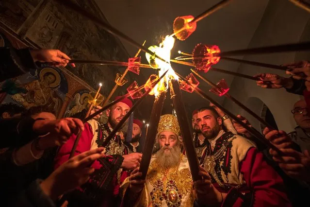 Orthodox pilgrims light candles from a torch burning with the Holy Fire from Jerusalem during the Orthodox Christian Easter service led by Bishop Partenie (C) at the 10th century monastery of St. John the Baptist “Sv. Jovan Bigorski” near Mavrovo, Republic of North Macedonia, 24 April 2022. (Photo by Georgi Licovski/EPA/EFE)