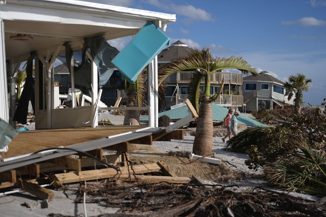 Resident Kerry Flynn, right, and a friend walk past a damaged home and the displaced roof of their 55+ mobile home community's tiki hut after the passage of Hurricane Milton, on Manasota Key, in Englewood, Fla., Sunday, October 13, 2024. (Photo by Rebecca Blackwell/AP Photo)