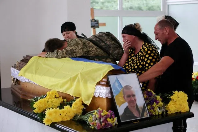 Relatives and guests mourn by the flag-draped coffin at the funeral of service member Taras Mykytsei, after he was killed in combat with invading Russian troops near Lysychansk, Luhansk region, at the city cemetery in Ivano-Frankivsk, Ukraine on July 6, 2022. (Photo by Yuriy Rylchuk/Reuters)