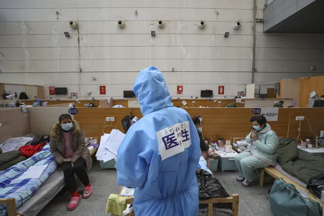 In this Friday, February 21, 2020, photo, a doctor in a protective suit checks with patients at a temporary hospital at Tazihu Gymnasium in Wuhan in central China's Hubei province. China's leadership sounded a cautious note Friday about the country's progress in halting the spread of the new virus that has now killed more than 2,200 people, after several days of upbeat messages. (Photo by Chinatopix via AP Photo)