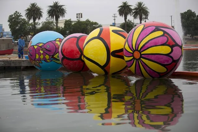Volunteer Aaron Diaz holds inflated spheres after they were lowered into MacArthur Park Lake during the installation of Portraits of Hope's exhibition “Spheres at MacArthur Park” in Los Angeles, California August 21, 2015. (Photo by Mario Anzuoni/Reuters)