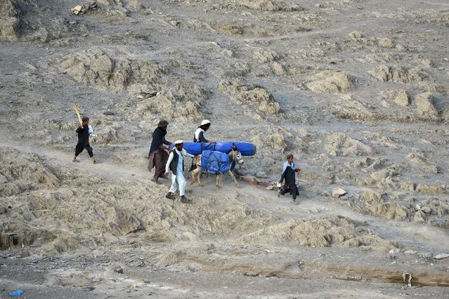 In this picture taken on June 26, 2022, volunteers carry aid being received from the International Organization for Migration (IOM) for recent earthquake affected people in the Afghan-Dubai village of Spera district in Khost province. In Afghan-Dubai – named at a time when the pine nut trade flourished in the coniferous mountainous region – the distribution of aid is strictly supervised by armed Afghan Taliban. (Photo by Ahmad Sahel Arman/AFP Photo)