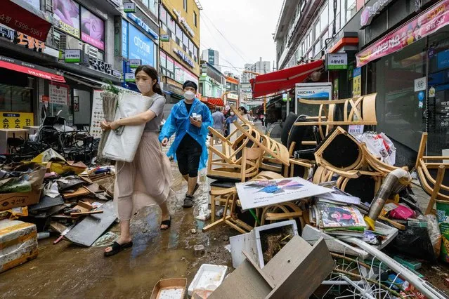 Pedestrians walk past debris outside shops at the historic Namseong Market in the Gangnam district of Seoul on August 9, 2022, after record-breaking rains caused severe flooding, with at least seven people dead and seven more missing, officials said. (Photo by Anthony Wallace/AFP Photo)