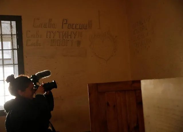 A media member films a cell at a preliminary detention centre, which, as Ukrainians say, was used by Russian service members to jail and torture people, before they retreated from Kherson, Ukraine on November 16, 2022. The slogans in Russian on the wall read: “Glory to Russia !!! Glory to Putin !!!, Glory to Shoigu !!!”. (Photo by Murad Sezer/Reuters)