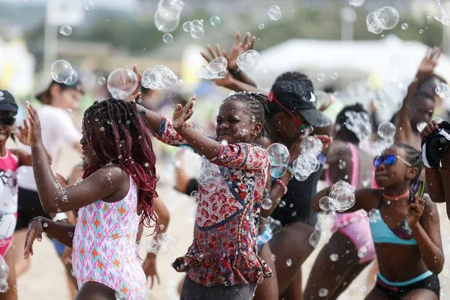 Children play with soap bubble along the beach in Deauville, northwestern France, on August 23, 2017 as part of the “Forgotten by the Holidays” campaign organised by the French NGO Secours Populaire for children whose families can not afford to go on holidays. (Photo by Charly Triballeau/AFP Photo)
