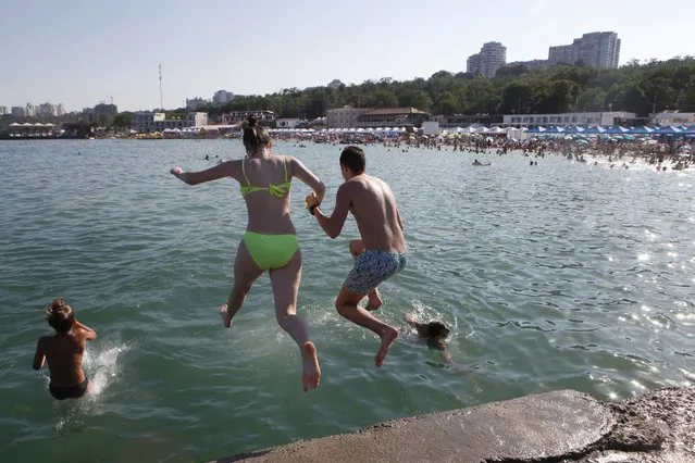 A couple jump into a water as they enjoy the beach in the Black Sea in Odessa, Ukraine, Saturday, July 4, 2020. Tens of thousands of vacation-goers in Russia and Ukraine have descended on Black Sea beaches, paying little attention to safety measures despite levels of contagion still remaining high in both countries. (Photo by Sergei Poliakov/AP Photo)