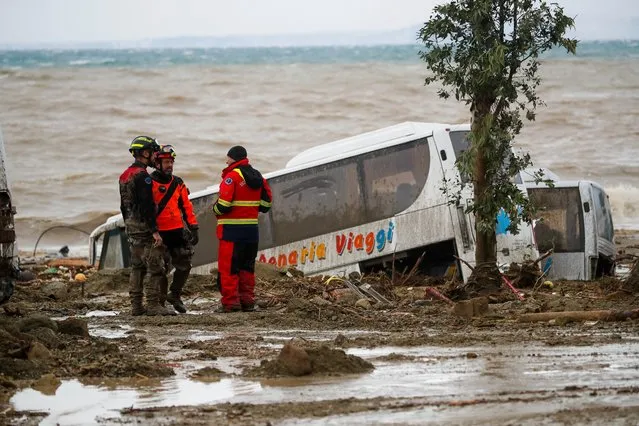 Rescuers stand next to a bus carried away after heavy rainfall triggered landslides that collapsed buildings and left as many as 12 people missing, in Casamicciola, on the southern Italian island of Ischia, Italy, Saturday, November 26, 2022. Firefighters are working on rescue efforts as reinforcements are being sent from nearby Naples, but are encountering difficulties in reaching the island either by motorboat or helicopter due to the weather. (Photo by Salvatore Laporta/AP Photo)