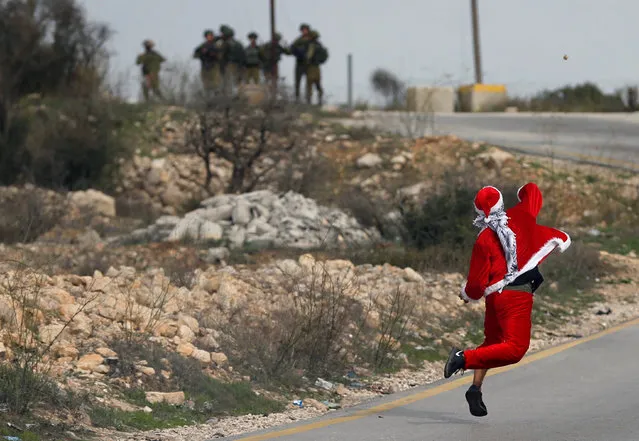 A Palestinian demonstrator dressed as Santa Claus hurls stones towards Israeli troops during clashes at a protest against U.S. President Donald Trump's decision to recognize Jerusalem as the capital of Israel, near the West Bank city of Ramallah December 19, 2017. (Photo by Mohamad Torokman/Reuters)