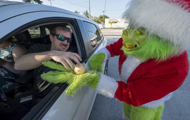 In this photo provided by the Florida Keys Press Office, a motorist accepts an onion in lieu of a traffic ticket from Monroe County Sheriff's Department Colonel Lou Caputo, disguised as the Grinch, the Tuesday, December 13, 2022 in Marathon, Florida. (Photo by Andy Newman/Florida Keys News Bureau via AP Photo)
