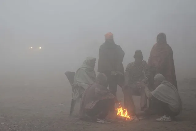 Indian labourers sit around a bonfire to warm up on a cold foggy morning at a wholesale vegetable market on the outskirts of Amritsar on January 3, 2018. (Photo by Narinder Nanu/AFP Photo)