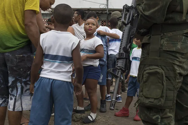 A young student looks at a Brazilian marine as she and her classmates have their bags inspected during a surprise operation in Kelson's slum in Rio de Janeiro, Brazil, Tuesday, February 20, 2018. (Photo by Leo Correa/AP Photo)