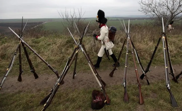 A historical re-enactment enthusiast dressed as a soldier walks past rifles near the southern Moravian village of Herspice November 28, 2014. (Photo by David W. Cerny/Reuters)