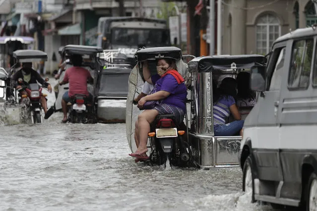 A woman wearing a mask to prevent the spread of the coronavirus rides a motorcycle as they pass a flooded street due to Typhoon Molave in Pampanga province, northern Philippines on Monday, October 26, 2020. (Photo by Aaron Favila/AP Photo)