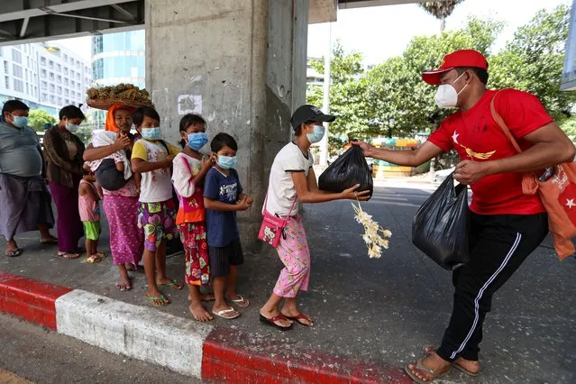 A supporter of Myanmar Leader Aung San Suu Kyi's National League for Democracy (NLD) party distributes food supplies to street vendors and children near a traffic junction during their movement for people's awareness for the upcoming Nov. 8 general election, Thursday, October 22, 2020, in Yangon, Myanmar. (Photo by Thein Zaw/AP Photo)
