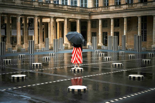 A woman with an umbrella poses on “Les Deux Plateaux”, commonly known as “Columns of Buren”, by French artist Daniel Buren and architect Patrick Bouchain, in the main courtyard of the Palais-Royal in central Paris on July 21, 2025. (Photo by Dimitar Dilkoff/AFP Photo)