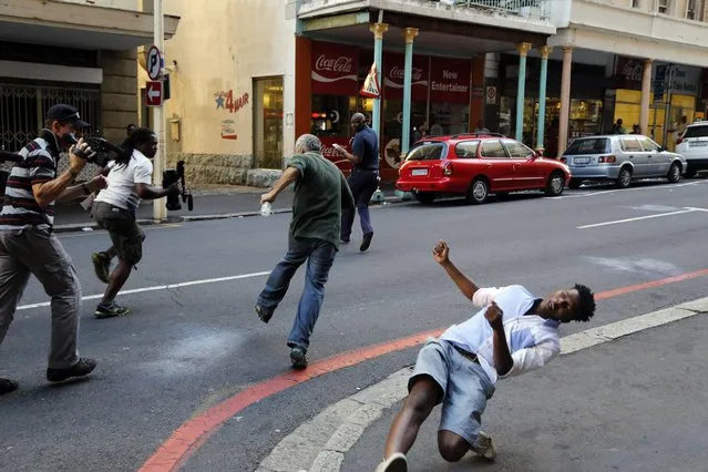 A student protestor, right, is hit by a rock thrown by a fellow protestor in Cape Town, South Africa, Wednesday, October 26, 2016.South African police have used stun grenades to disperse student protesters outside parliament, where the finance minister was giving a budget speech. (Photo by Schalk van Zuydam/AP Photo)