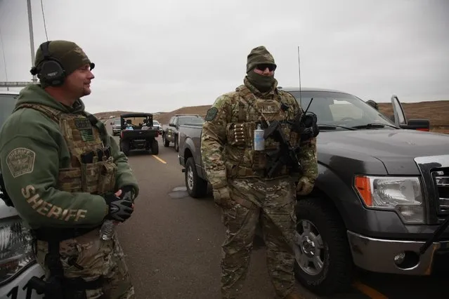 Two members of the Stutsman County SWAT team talk while deployed to watch protesters demonstrating against the Dakota Access Pipeline encroaching the water source near the Stand Rock Sioux Reservation, as they stand next to a police barricade on Highway 1806 in Cannon Ball, N.D., Sunday, October 30, 2016. (Photo by John L. Mone/AP Photo)