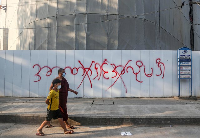 A Buddhist monk and a boy walk in front of a graffiti that reads “We don't want a dictator” following a protest against military coup in Yangon, Myanmar ob February 4, 2021. (Photo by Reuters/Stringer)