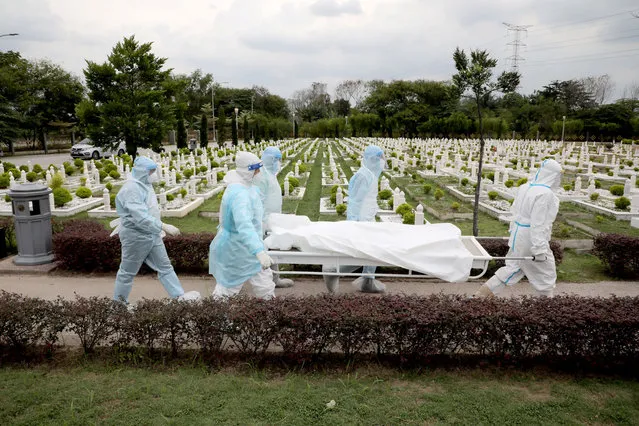 Workers wearing personal protective equipment (PPE) carry the body of a victim of the coronavirus disease (COVID-19) at a cemetery, in Batu Caves, Malaysia on January 27, 2021. (Photo by Lim Huey Teng/Reuters)