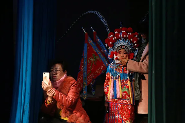 A participant waits for her turn backstage as a woman takes pictures of a performance during a traditional Chinese opera competition at the National Academy of Chinese Theatre Arts in Beijing, China, November 26, 2016. (Photo by Thomas Peter/Reuters)