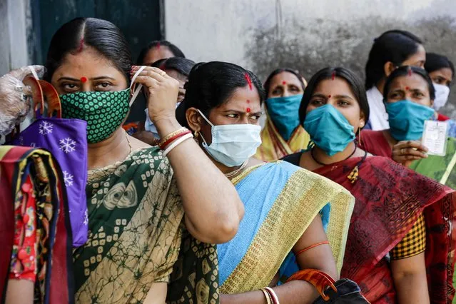 A woman adjusts her facemark as she stands in queue with others to cast their votes at a polling booth during the second phase of elections for West Bengal state in Nandigram , East Medinipur district, India, Thursday, April 1, 2021. (Photo by Bikas Das/AP Photo)