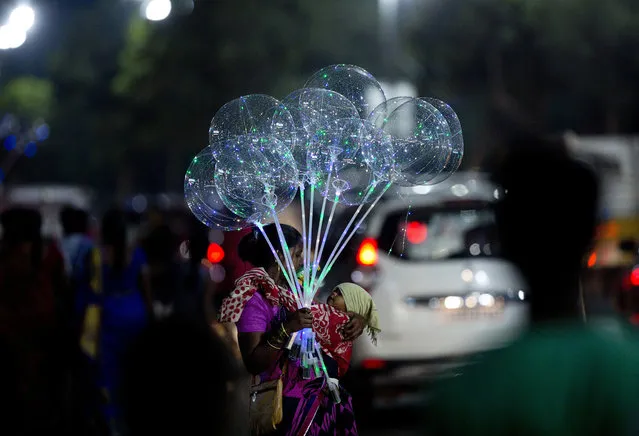 An Indian vendor carries an infant and stands on a street selling balloons in Hyderabad, Friday, September 21, 2018. (Photo by Mahesh Kumar A./AP Photo)