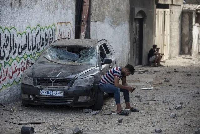 A Palestinian man sits on a damaged car following Israeli airstrikes on Jabaliya refugee camp, northern Gaza Strip, Thursday, May 20, 2021. Heavy airstrikes pummeled a street in the Jabaliya refugee camp in northern Gaza, destroying ramshackle homes with corrugated metal roofs nearby. The military said it struck two underground launchers in the camp used to fire rockets at Tel Aviv. (Photo by Khalil Hamra/AP Photo)