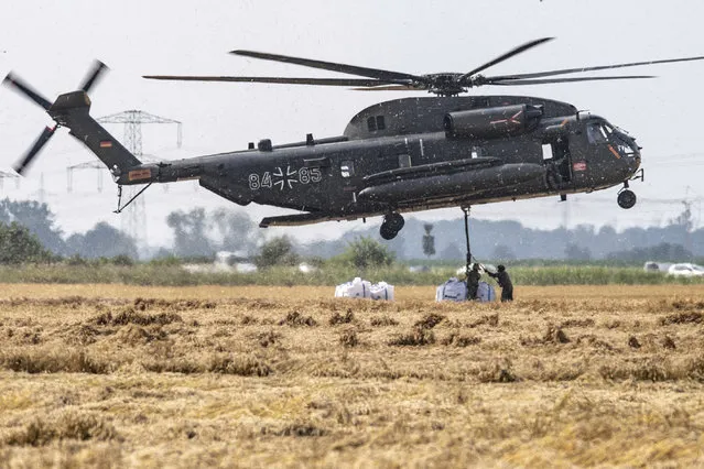 A Bundeswehr CH-53 transport helicopter picks up big bags of ballast in Ergfstadt, Germany, Thursday July 22, 2021, to fly them to the Blessem district to damn up the banks of the Erft river. In the flood disaster area of Erftstadt-Blessem, some residents are being allowed back into their homes to clear debris after heavy rains caused devastating floods. (Photo by Marius Becker/dpa via AP Photo)