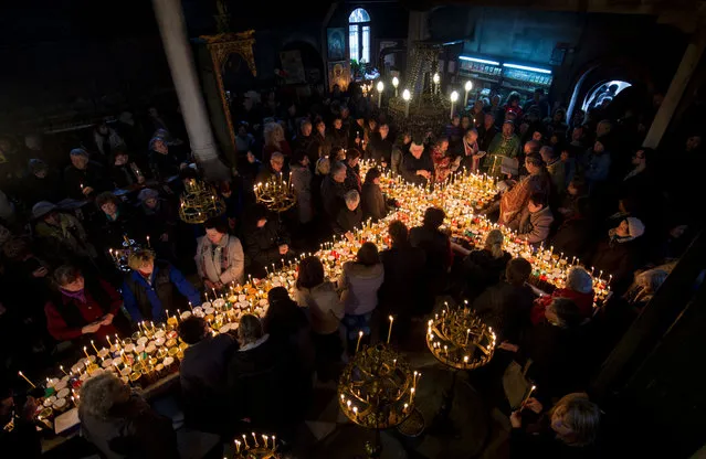 Bulgarian Orthodox faithfuls light candles with jars of honey during a holy mass for the “sanctification of honey” at the Presentation of the Blessed Virgin church in the town of Blagoevgrad, Bulgaria, 10 February 2016. Honey and beehives are sanctified by performing a ritual for health and rich harvest. On St. Haralambos' Day, sick or blind people go to church and pray for healing. According to traditional concepts, St. Haralambos is the lord of all illnesses, especially the plague. (Photo by Vassil Donev/EPA)