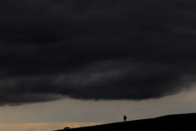 A man walks his dog under storm clouds on the Curragh race track, in Newbridge, Ireland on August 16, 2023. (Photo by Clodagh Kilcoyne/Reuters)