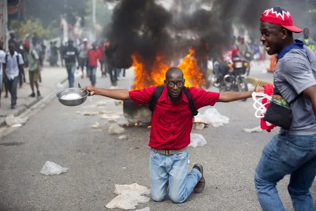 A demonstrator kneels in front of a burning barricade holding a bowl and spoon to show his hunger, during a protest to demand the resignation of President Jovenel Moise and demanding to know how Petro Caribe funds have been used by the current and past administrations, in Port-au-Prince, Haiti, Thursday, February 7, 2019. (Photo by Dieu Nalio Chery/AP Photo)