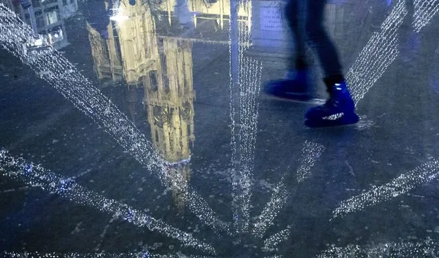 A skater skates through the reflection of the Antwerp Cathedral on the water of an ice skating rink at a Christmas market in the historical Grote Markt of Antwerp, Belgium on Tuesday, December 22, 2015. Warmer than normal temperatures for December caused the ice skating rink to melt. (Photo by Virginia Mayo/AP Photo)