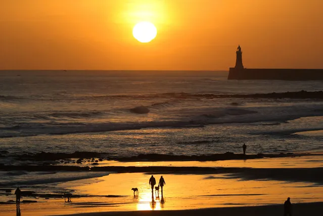 Walkers take a stroll along the beach at sunrise in Tynemouth Longsands, UK on December 27, 2016. (Photo by Owen Humphreys/AP Photo)