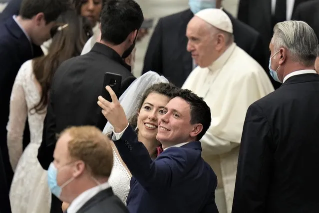 A newlywed couple takes a selfie as Pope Francis leaves at the end of his weekly general audience in the Paul VI Hall, at the Vatican, Wednesday, November 10, 2021. (Photo by Alessandra Tarantino/AP Photo)
