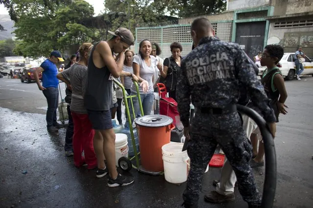 A woman complains that someone bumped ahead of her in line as a Bolivarian policeman fills a resident's container with water, in Caracas, Venezuela, Monday, April 1, 2019. Since a massive power failure struck March 7, the nation has experienced near-daily blackouts and a breakdown in critical services such as running water and public transportation. (Photo by Ariana Cubillos/AP Photo)